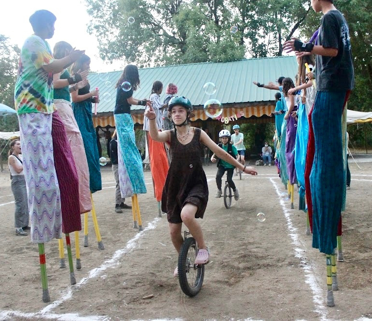 Unicyclists riding through a column of stilt walkers